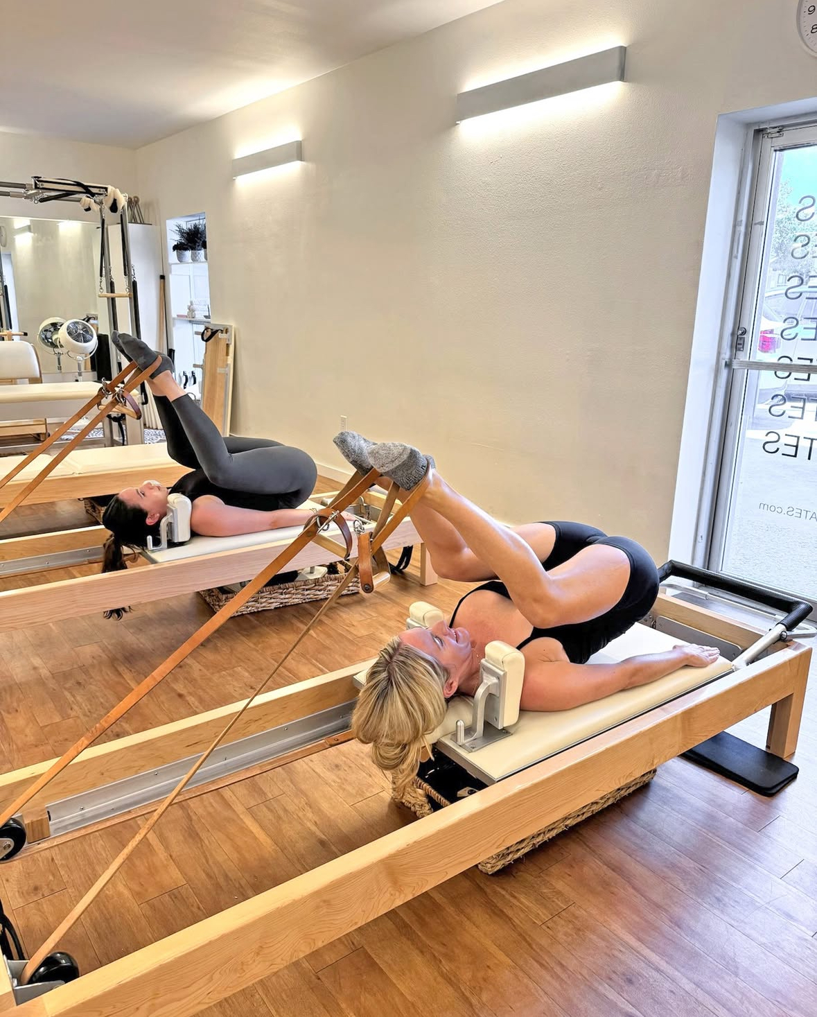 Two women performing classical Pilates leg spring exercises on Reformers at Sharp Pilates studio in Austin, TX, showcasing strength, control, and precise alignment in a bright, minimalist space.